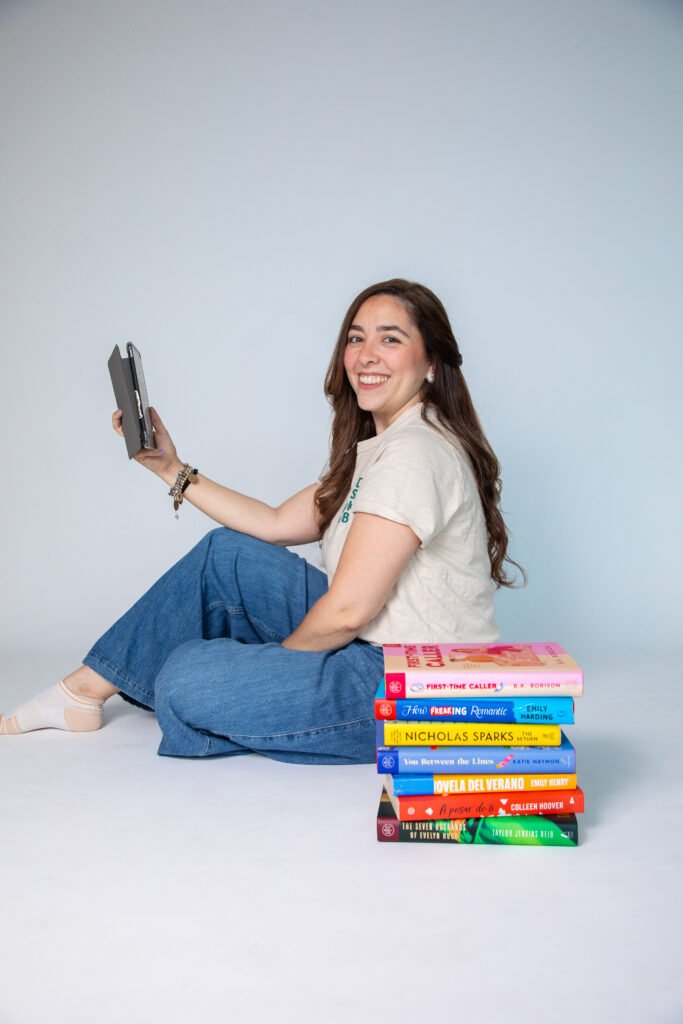 Teacher Ame leyendo en un lector digital junto a una pila de libros
